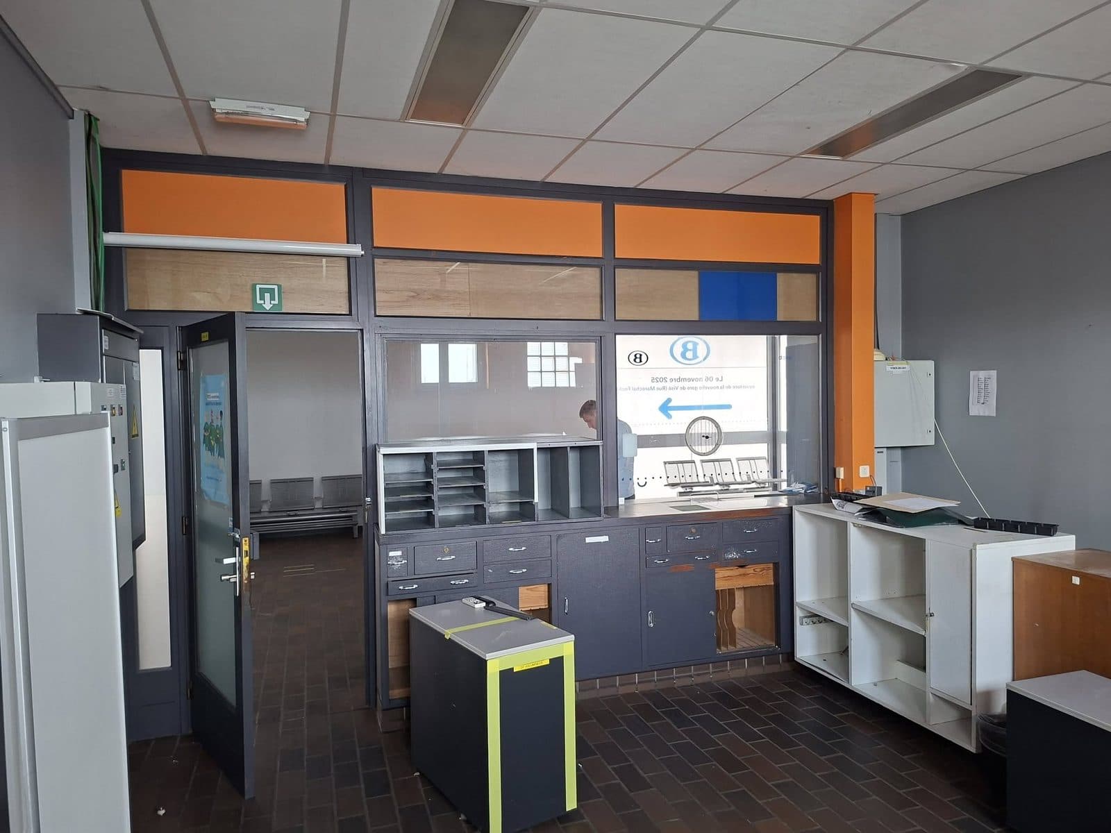 La salle avant les travaux : les guichets vitrés de la gare, le carrelage brun et les panneaux orange