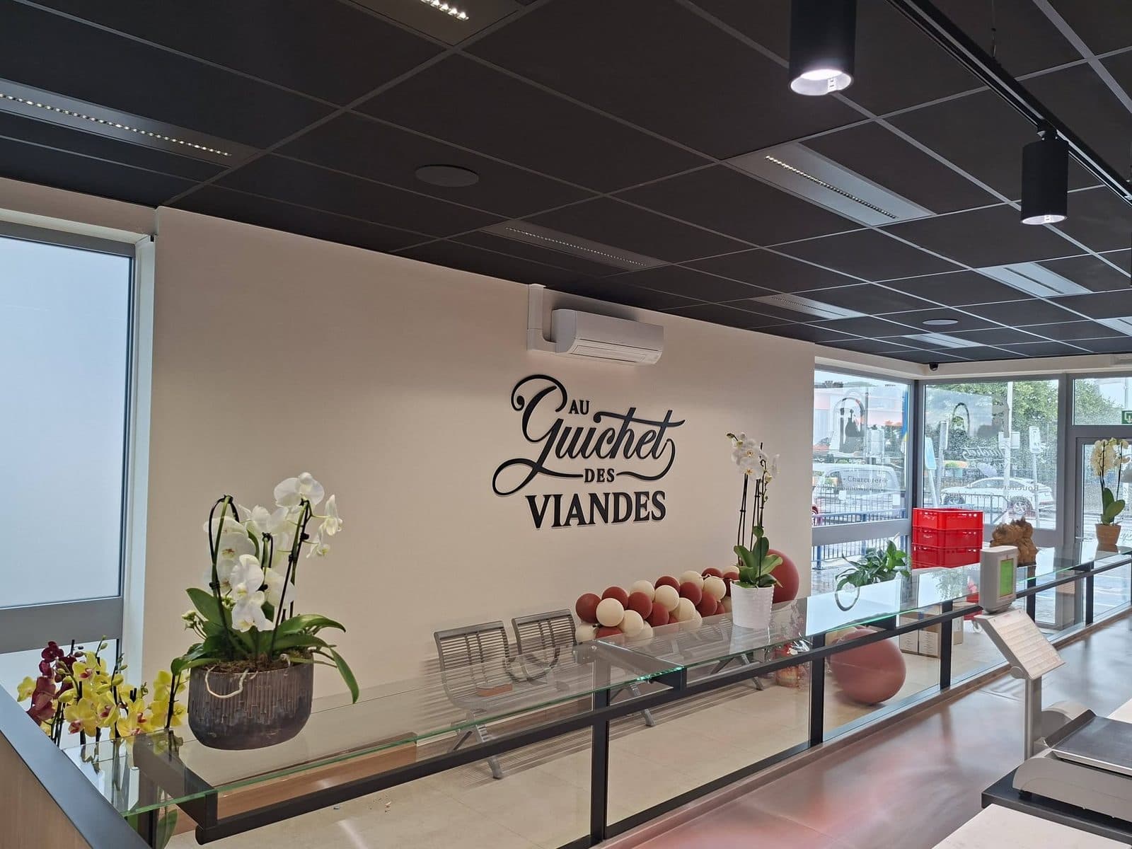 L'entrée de la boutique, le nom Au Guichet des Viandes peint au mur et des orchidées sur le comptoir